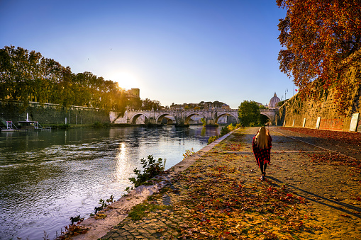 A warm autumn sunset illuminates the Tiber bank in the heart of Rome, creating a unique pictorial atmosphere by pastel colors. In the background stands the majestic silhouette of the dome of St. Peter's and Ponte Sant'Angelo. Image in High Definition format.