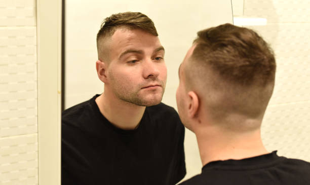 istock Young man looking in the mirror at his reflection in a bathroom 1298077560