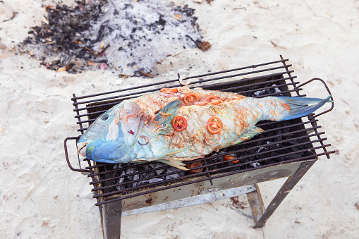 Fresh tropical fish with vegetables cooking outdoor on the beach grill. Charcoal stove, tropical food, exotic food.