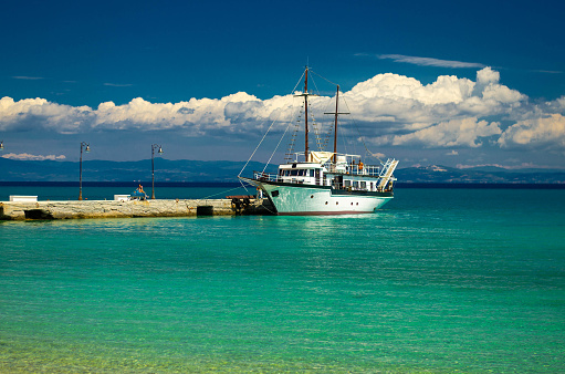 Pefkohori, Greece, May 17, 2016: View of ship boat on blue paradise water of Toroneos kolpos gulf, blue sky, white clouds over Sithonia peninsula near pier