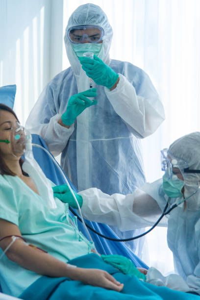 Los médicos en traje protector vacunan y monitorean la presión arterial del paciente infectado con CORONA VISRUS o COVID-19 en la sala de cuarentena del hospital. - foto de stock