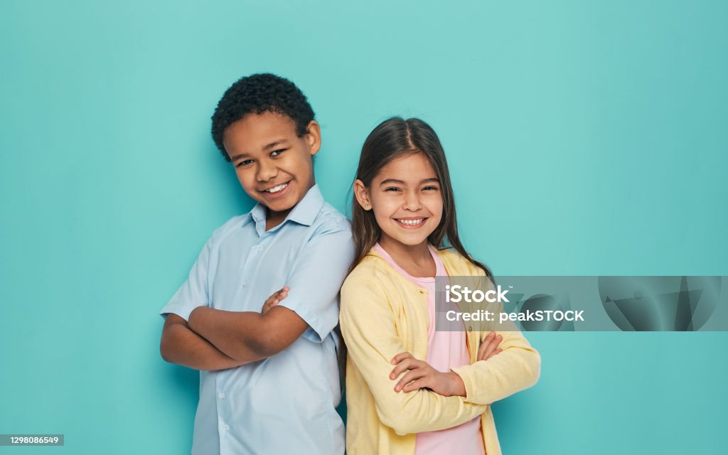 Asian girl and African American boy standing back to back with arms crossed on a turquoise background Child Stock Photo