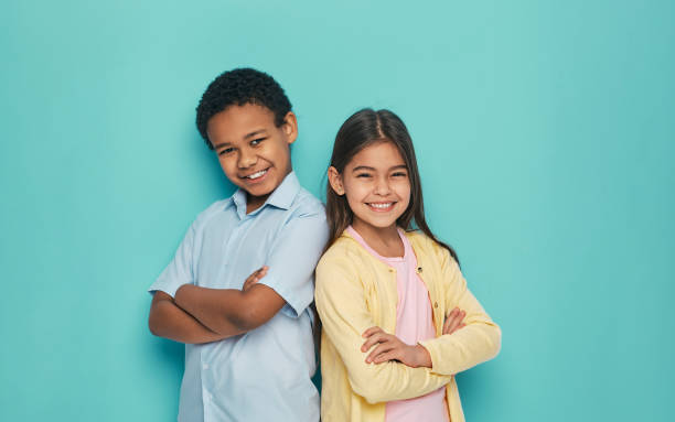 Asian girl and African American boy standing back to back with arms crossed on a turquoise background Asian girl and African American boy standing back to back with arms crossed on a turquoise background 6 7 years stock pictures, royalty-free photos & images