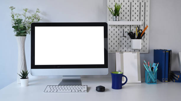 istock Front view of mock up computer with blank screen and office supplies on white table at stylish work place. 1298092741