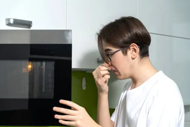 a man smells an unpleasant smell from the microwave in the kitchen