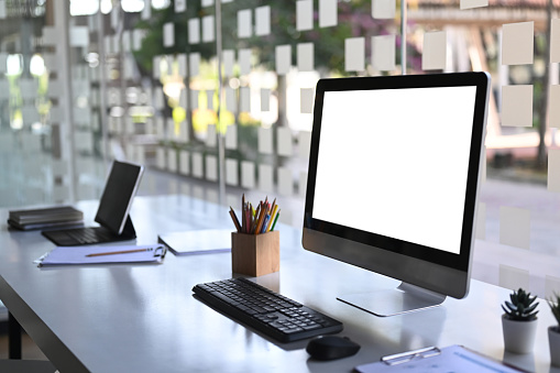 Side view of computer with blank screen and tablet on modern workstation.