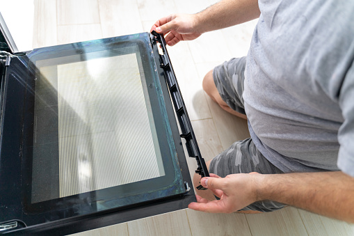 the man removes the fireproof glass from the oven. repair and cleaning of an electric oven