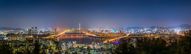 Highrise cityscape and glittering neon night skyscrapers along the tranquil waters of the Han River in the heart of Seoul, South Korea’s vibrant capital city.
