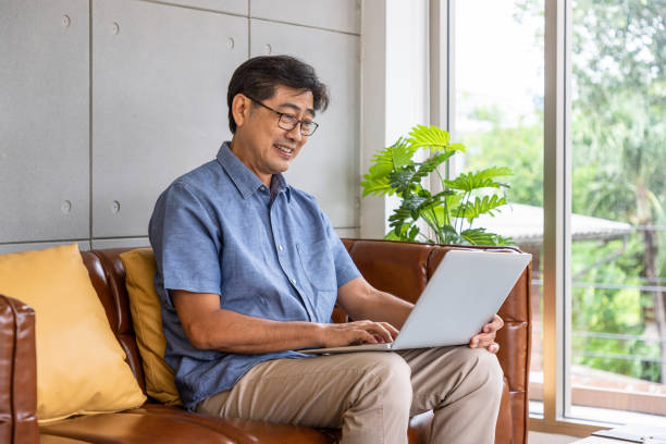 istock Happy Asian senior retired man sitting on couch sofa, using laptop computer 1298098232