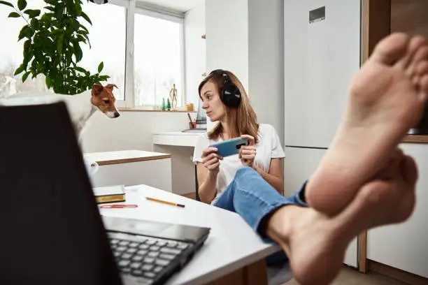 Photo of Woman listening online course in headphones, distance education. Freelancer sitting at workplace and procrastinating. Lazy and distracted employee at remote work