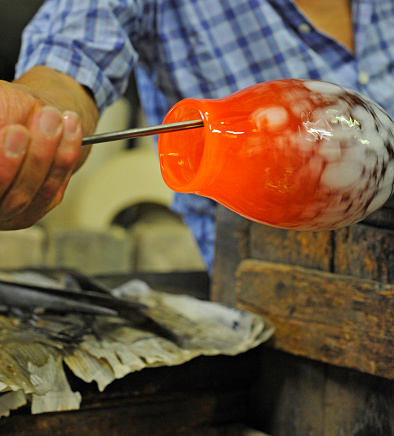 Close up of artisan hand forging hot glass into a vase in Murano, Venice.