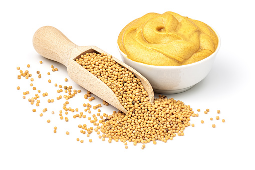 Mustard seeds in the wooden scoop and mustard sauce in the bowl isolated on white background.
