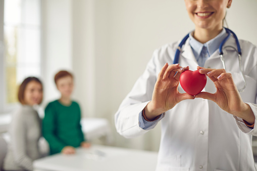 Happy family doctor holding red heart. Good health, cardiology, heart conditions prevention, healthy lifestyle promotion, human organ donation, implantation concept. Blurred background, space for text