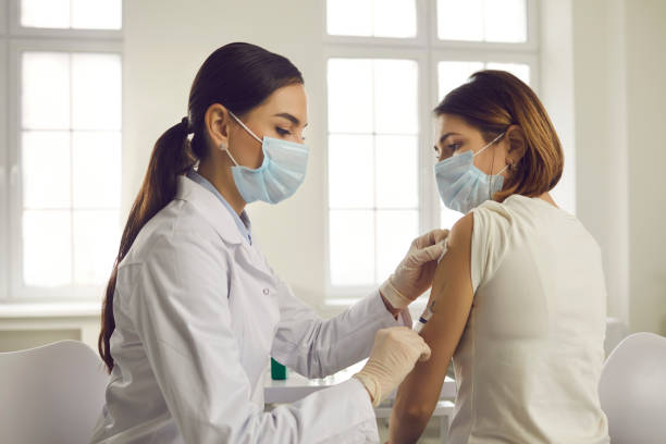 молодая женщина в маске для лица получает противовирусную вакцину в больнице или поликлинике - injecting syringe vaccination doctor стоковые фото и изображения