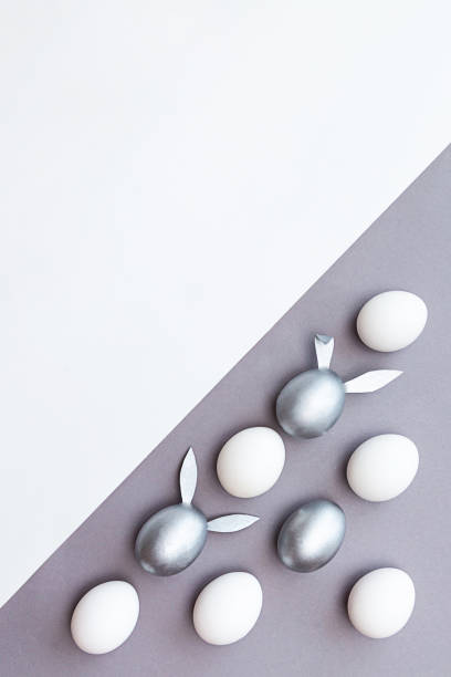 istock Minimal concept for Easter. Eggs with bunny ears are colored silver and white eggs on a white and gray background 1298110555