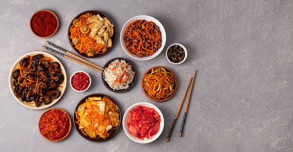 Assorted Korean pickled salads and fermented vegetables in plates on a gray background with chopsticks. Copy space, flat lay