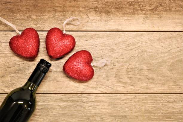 Three red glitter hearts surround the top of a wine bottle on a wood background.