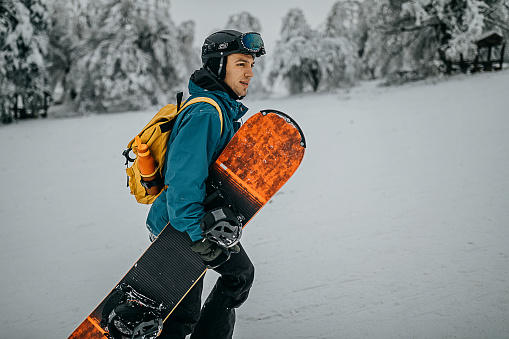 Young man carrying snowboard and enjoying winter on the mountain