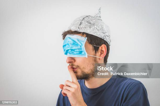 Conspiracy Theory Concept Young Man With Face Mask Over The Eyes And Aluminum Hat Is Making A Psst Gesture Stock Photo - Download Image Now