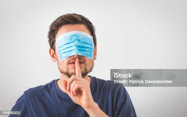 Conspiracy Theory Concept Young Man With Face Mask Over The Eyes Is Making A Psst Gesture Stock Photo - Download Image Now