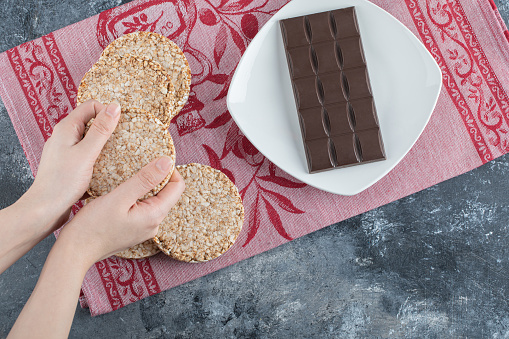 Woman hands holding crispy rice bread with bar of chocolate . High quality photo