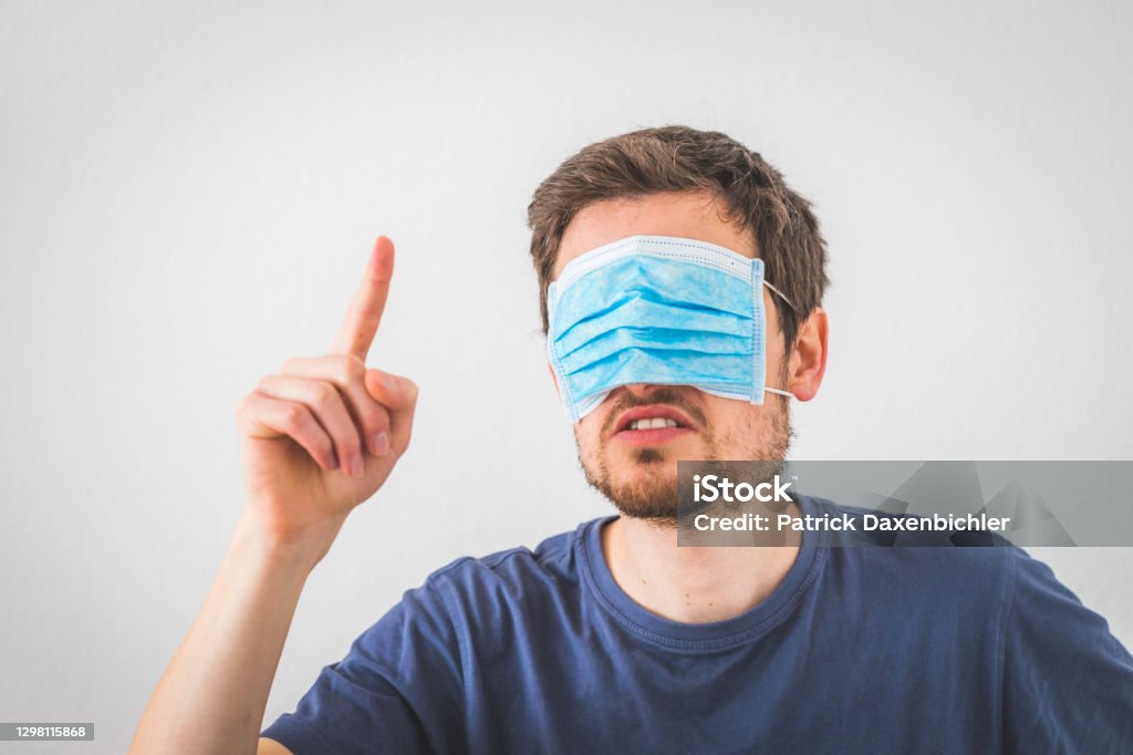 Conspiracy theory concept: Young angry man is wearing face mask over the eyes, gesturing angry. Young angry man is wearing face mask over the eyes and gesturing angry. Conspiracy theory concept. Coronavirus Stock Photo