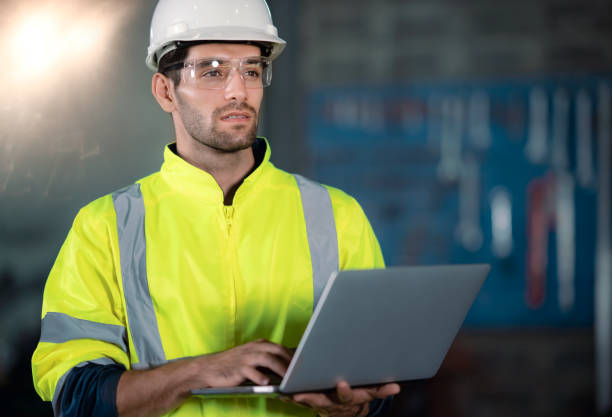 istock Chief Engineer in the Hard Hat Walks Through Light Modern Factory While Holding Laptop 1298116162