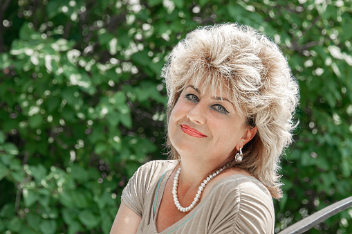 Portrait of a beautiful Mature blonde sitting on a bench. The woman smiles and looks at the camera. Copy space.