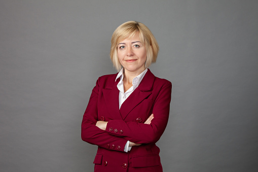 Studio portrait of 45 year old blonde woman in maroon business suit on gray background