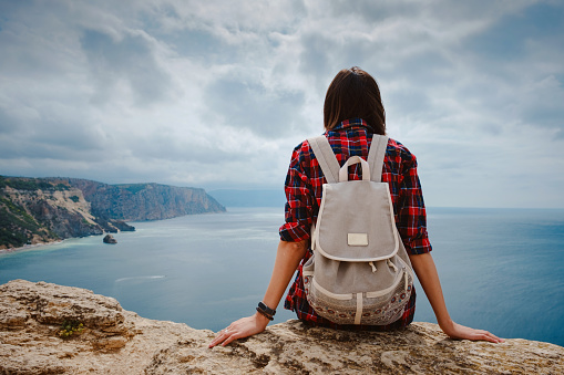 woman traveling with backpack tourist on seashore in summer. Enjoying Beautiful clouds sky among Mighty Cliffs Meeting Ocean. the idea and concept of freedom, vacation and discovery