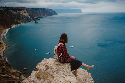 woman traveling with backpack tourist on seashore in summer. Enjoying Beautiful clouds sky among Mighty Cliffs Meeting Ocean. the idea and concept of freedom, vacation and discovery