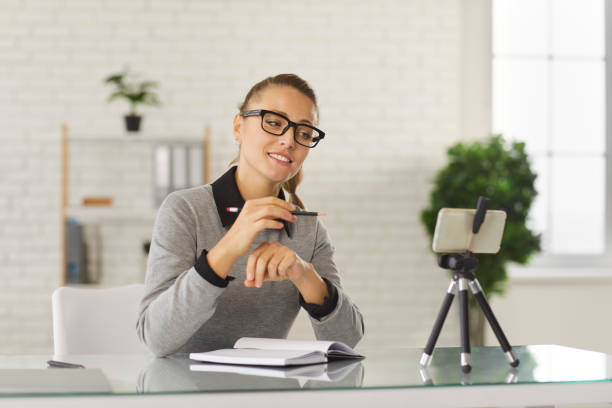 istock Young woman office worker looking at smartphone camera making notes during teleconference 1298127401