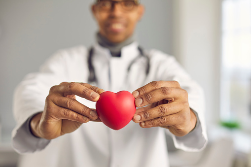 African doctor holding red heart. Selective focus, man's hands in close-up. Concept of good health, cardiovascular diseases prevention, healthy lifestyle promotion, human organ donation, implantation