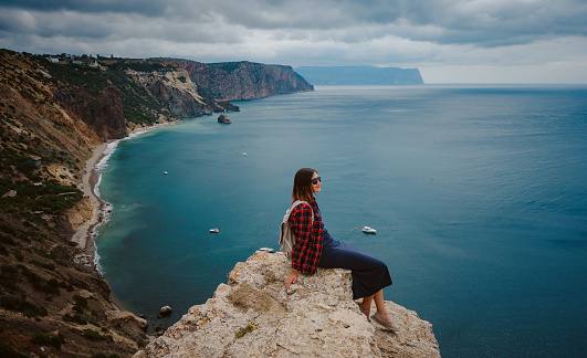 woman traveling with backpack tourist on seashore in summer. Enjoying Beautiful clouds sky among Mighty Cliffs Meeting Ocean. the idea and concept of freedom, vacation and discovery