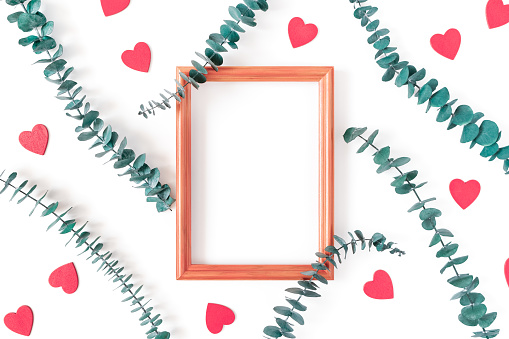 Eucalyptus branches, red wooden figurines in the shape of a heart and an empty wooden photo frame are on a white background. Composition for Valentine's Day. Flat lay. Top view. Copy space.