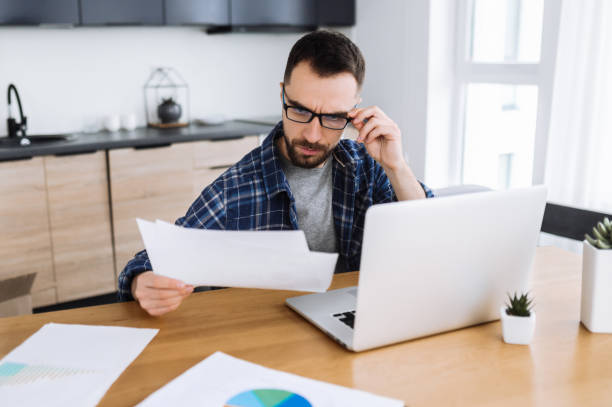 istock Busy freelancer man doings paper work remotely, develop a project or startup. Caucasian male entrepreneur wearing eyeglases look at the financial graphs, learn some information, develops a strategy. Distant work concept 1298133513