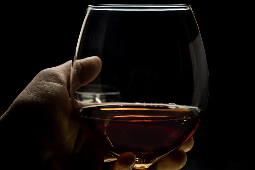 Glass with cognac in a man's hand on a black background, expensive cognac in his hand. Cognac tasting.