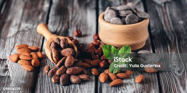 Cocoa Beans Almonds Hazelnuts Chocolate And Mint Leaves On A Dark Wooden Table Selective Focus Banner Stock Photo - Download Image Now
