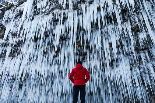 Man in red jacket watching a spectacular frozen waterfall (Pericnik, Slovenia).