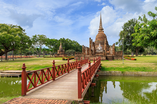 Red wooden bridge across the pond leading to pagoda and ruined chapel monastery complex at Wat Sa Si temple, Sukhothai Historical Park, Thailand