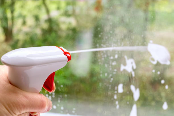 istock Cleaning window pane with spray detergent. Outside the window blurred street, greenery. Concept for home cleaning services 1298139556