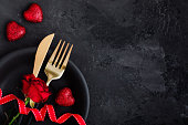Valentine's Day table setting with plate, gold knife, fork, red rose, ribbon and hearts
