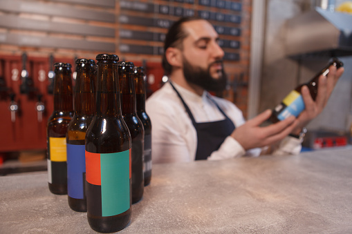 Selective focus on beer bottles on the counter, bartender examining beer bottle on background