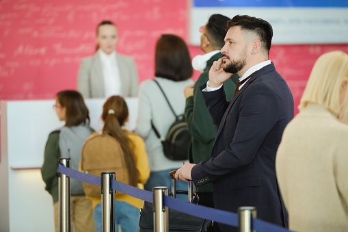 Young businessman in suit talking on mobile phone while standing in a queue and waiting for his registration