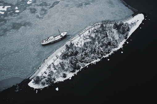 An abandoned ship that has broken from it's mooring and run aground on an island. Drone view with fresh snow.
