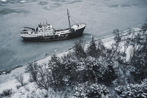 An abandoned ship that has broken from it's mooring and run aground on an island. Drone view with fresh snow.