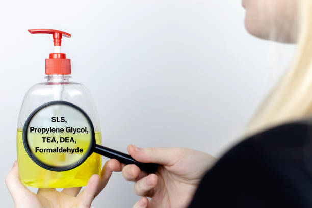 a woman examines the harmful ingredients of the liquid soap a magnifying glass. harmful composition of ingredients. means with sls, propylene glycol, tea, dea, formaldehyde. - propylene imagens e fotografias de stock