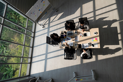 high angle view of office room with business people meeting and discussing at table with natural light from transparent window with green garden view