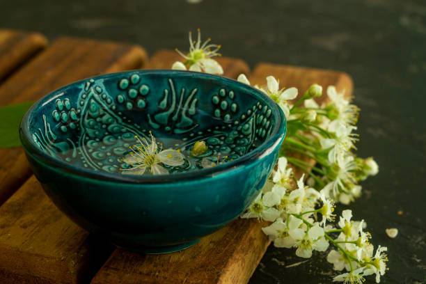 A blue oriental Turkish bowl with transparent water on a background of white cherry flowers on a wooden board and a black background. Copy space. Spring holiday concept.