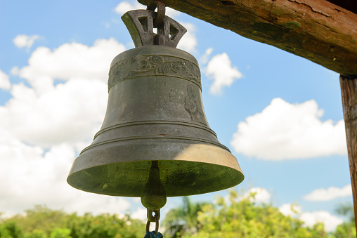 copper bell hanging with blue sky and clouds in the background.
